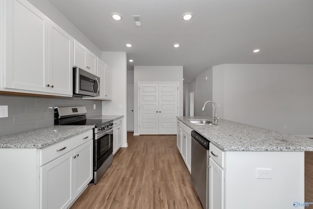 kitchen featuring sink, light stone counters, a center island with sink, appliances with stainless steel finishes, and white cabinets