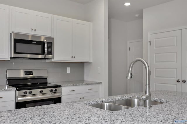 kitchen with light stone countertops, white cabinetry, appliances with stainless steel finishes, and sink