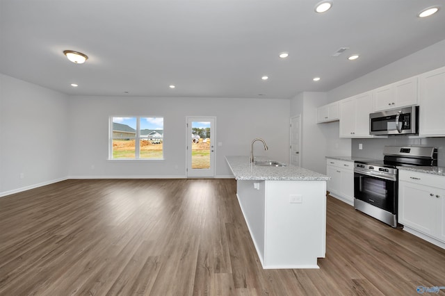 kitchen featuring sink, white cabinetry, stainless steel appliances, light stone counters, and a center island with sink