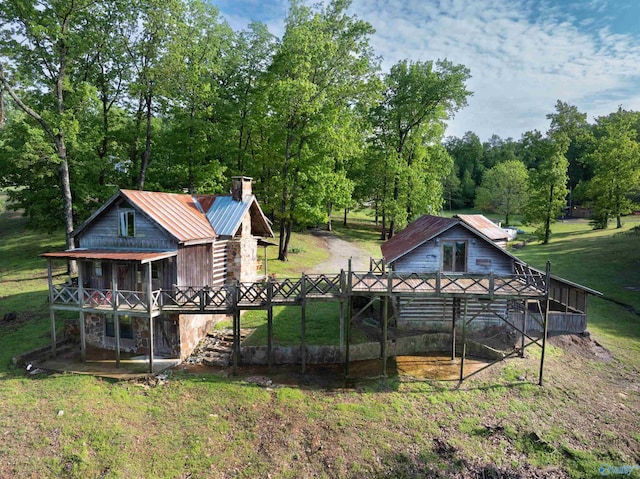rear view of house with a wooden deck, a yard, a chimney, and metal roof