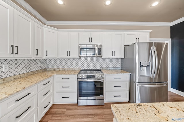 kitchen with stainless steel appliances, ornamental molding, light wood-type flooring, and white cabinetry