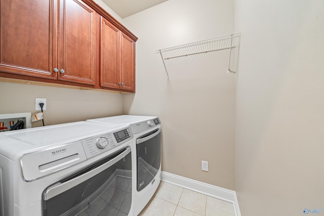 laundry area featuring light tile patterned flooring, washing machine and dryer, cabinet space, and baseboards