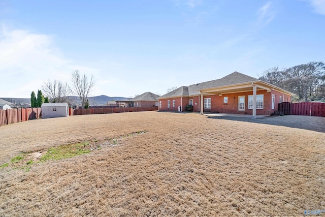 rear view of house featuring an outbuilding, brick siding, a fenced backyard, and a shed