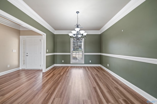 unfurnished dining area with a notable chandelier, crown molding, baseboards, and wood finished floors