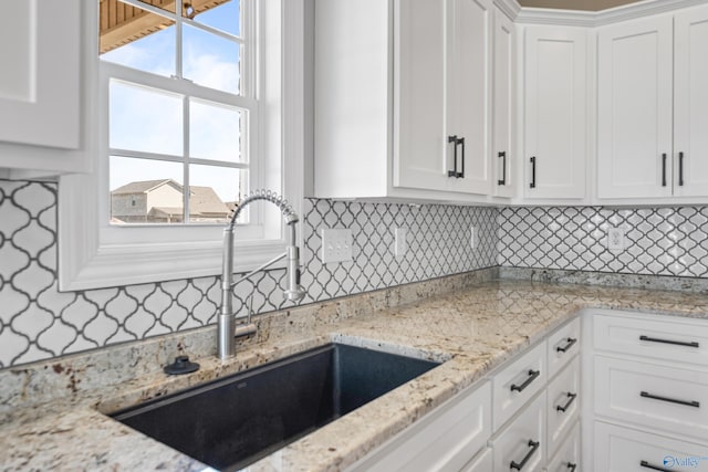 kitchen with light stone counters, white cabinets, a sink, and backsplash