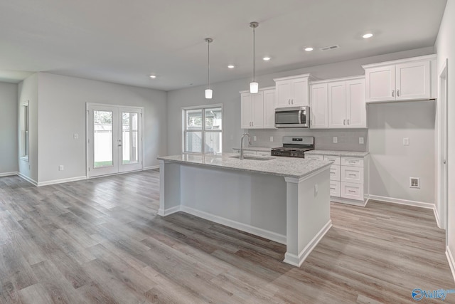 kitchen with a center island with sink, sink, appliances with stainless steel finishes, hanging light fixtures, and white cabinets