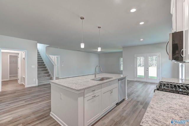 kitchen featuring decorative light fixtures, sink, light hardwood / wood-style floors, white cabinets, and a kitchen island with sink