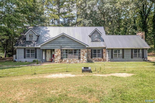 cape cod home featuring metal roof, a front lawn, a chimney, and stone siding