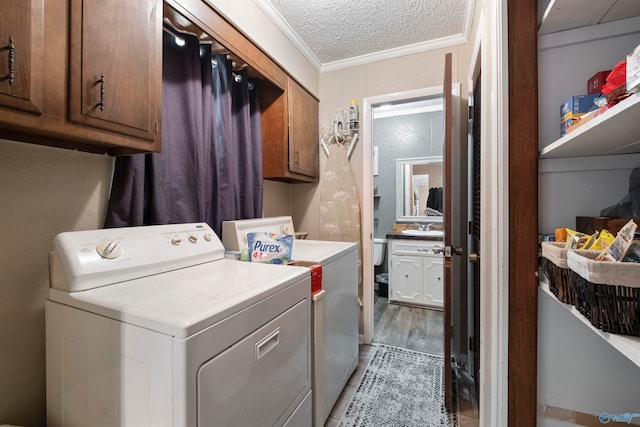 laundry area with cabinets, a textured ceiling, crown molding, light hardwood / wood-style floors, and washing machine and dryer