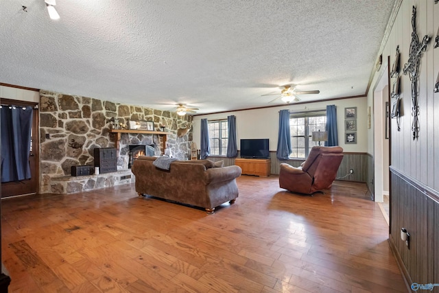 living room featuring crown molding, a textured ceiling, a stone fireplace, wood-type flooring, and ceiling fan