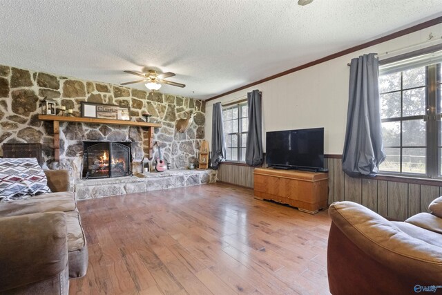 living room with crown molding, a textured ceiling, hardwood / wood-style floors, ceiling fan, and a fireplace