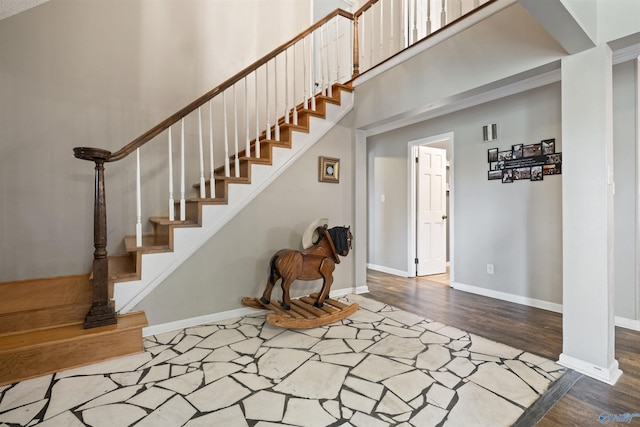 stairway with a high ceiling, wood finished floors, visible vents, and baseboards