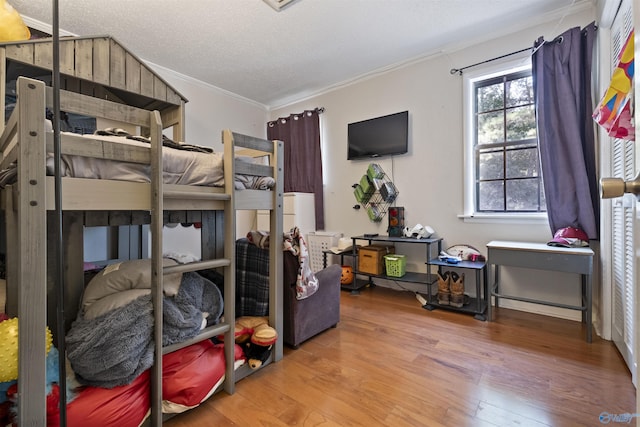 bedroom with a textured ceiling, ornamental molding, and wood finished floors