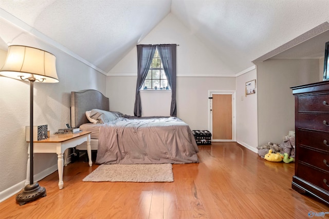 bedroom with vaulted ceiling, a textured ceiling, and hardwood / wood-style floors