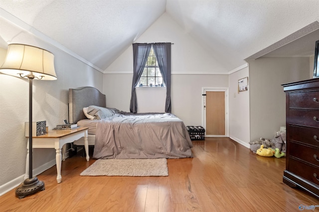 bedroom with vaulted ceiling, a textured ceiling, wood finished floors, and baseboards