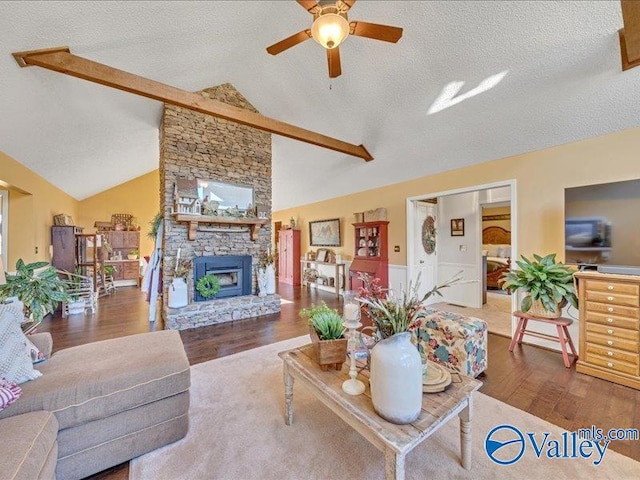 living room featuring hardwood / wood-style floors, a fireplace, vaulted ceiling with beams, ceiling fan, and a textured ceiling