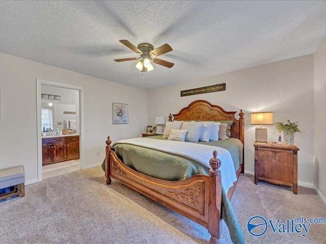 bedroom with a textured ceiling, ensuite bath, light colored carpet, and ceiling fan