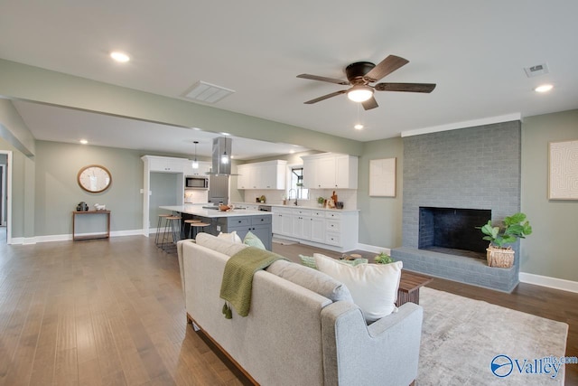 living room with hardwood / wood-style floors, a fireplace, sink, and ceiling fan