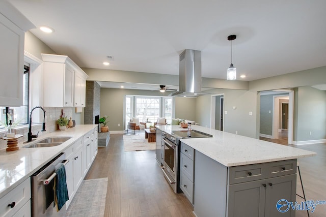 kitchen with sink, appliances with stainless steel finishes, white cabinetry, hanging light fixtures, and island range hood