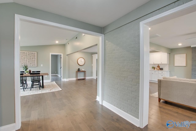 hallway with brick wall, wood-type flooring, and vaulted ceiling