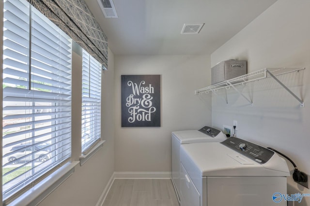 clothes washing area featuring washing machine and clothes dryer, visible vents, a healthy amount of sunlight, laundry area, and baseboards