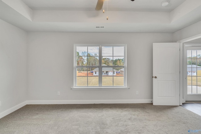 carpeted empty room with visible vents, ceiling fan, baseboards, and a tray ceiling