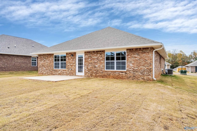 rear view of house featuring cooling unit, a shingled roof, a lawn, a patio area, and brick siding