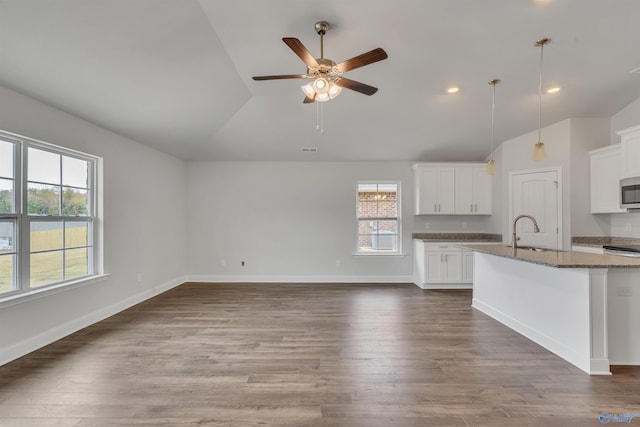 kitchen featuring lofted ceiling, a sink, stainless steel microwave, dark wood finished floors, and baseboards