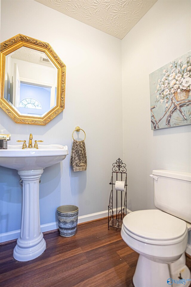 bathroom with a textured ceiling, wood-type flooring, and toilet