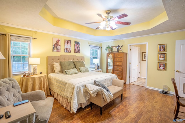 bedroom featuring multiple windows, a tray ceiling, ceiling fan, and hardwood / wood-style flooring