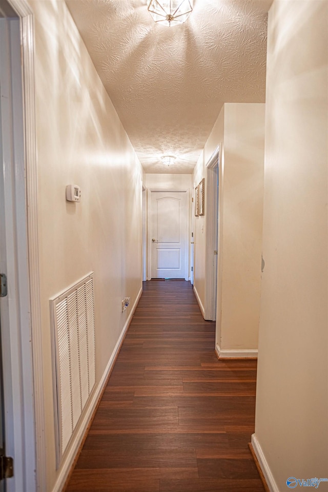 hallway with a textured ceiling and dark hardwood / wood-style floors