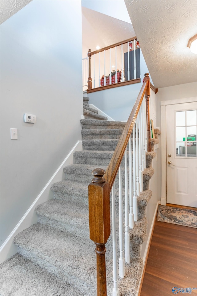 staircase featuring wood-type flooring, a textured ceiling, and lofted ceiling