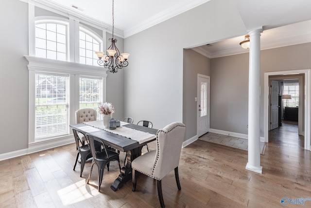 dining space featuring crown molding, a chandelier, light wood-type flooring, and ornate columns