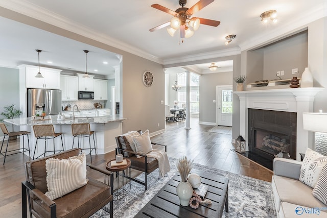 living room with sink, crown molding, light hardwood / wood-style flooring, ceiling fan, and a tiled fireplace