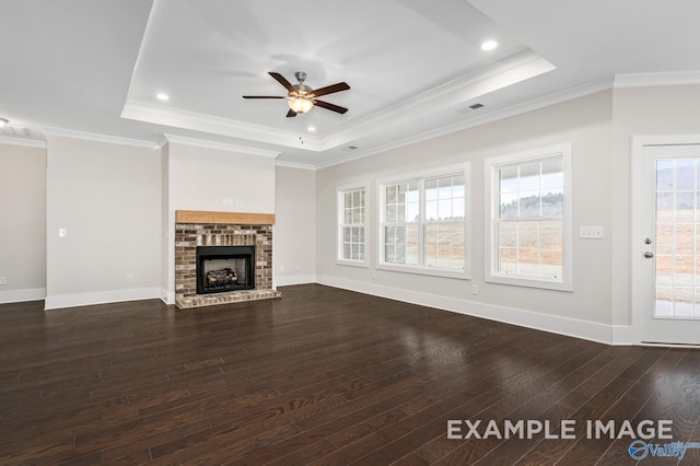 unfurnished living room with dark wood-style floors, a brick fireplace, a tray ceiling, and crown molding