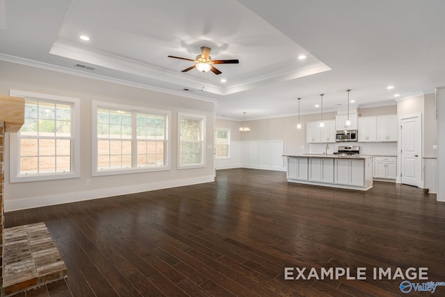 unfurnished living room featuring ceiling fan with notable chandelier, visible vents, ornamental molding, dark wood-style floors, and a raised ceiling