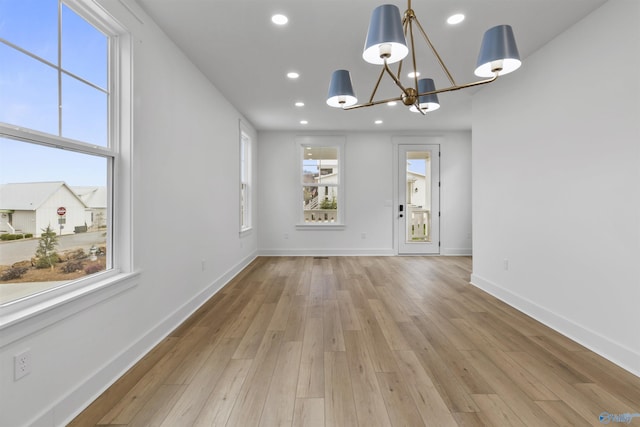 unfurnished dining area with recessed lighting, a notable chandelier, baseboards, and light wood-type flooring