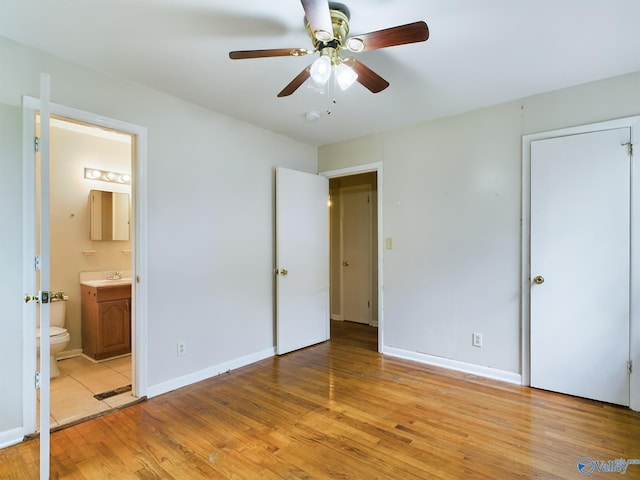 unfurnished bedroom featuring light wood-type flooring, ensuite bathroom, ceiling fan, and sink