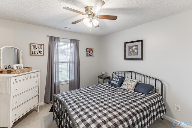 bedroom with ceiling fan, light colored carpet, and a textured ceiling