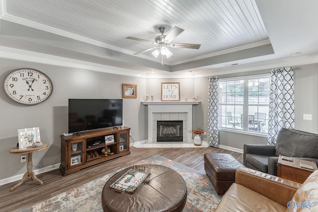 living room featuring ornamental molding, a tray ceiling, ceiling fan, a tile fireplace, and hardwood / wood-style floors