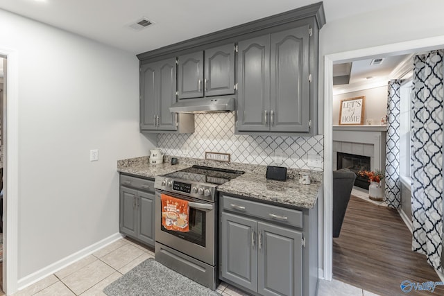 kitchen with stainless steel electric stove, gray cabinets, light wood-type flooring, a fireplace, and tasteful backsplash