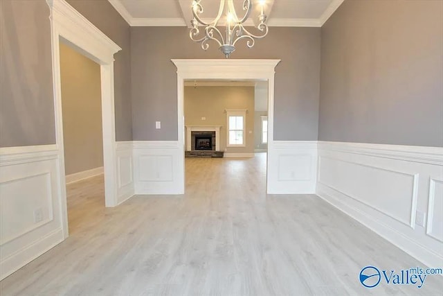 17401 Stonegate Dr, Athens, AL 35613 - unfurnished dining area with ornamental molding, a chandelier, light wood-style flooring, a stone fireplace, and a wainscoted wall