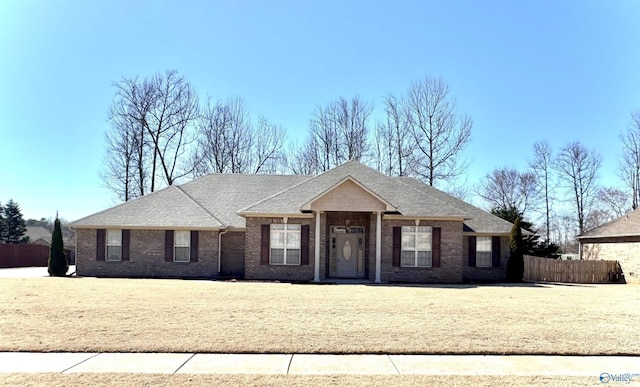 ranch-style house featuring brick siding, fence, and roof with shingles