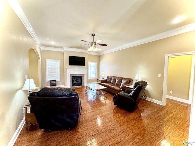 living area with crown molding, a tiled fireplace, baseboards, and wood finished floors