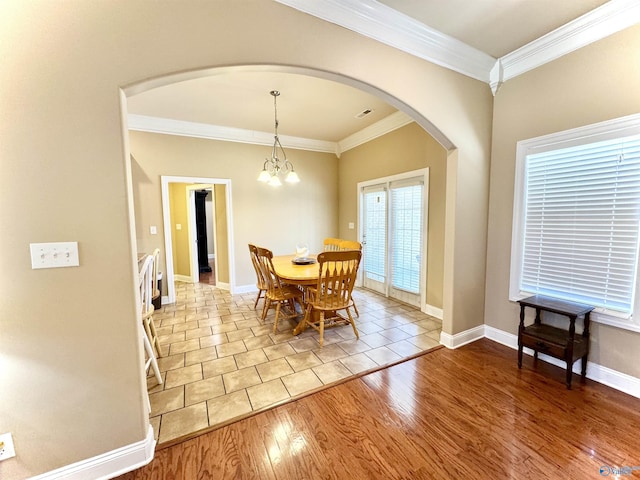 dining space with arched walkways, a notable chandelier, wood finished floors, baseboards, and crown molding