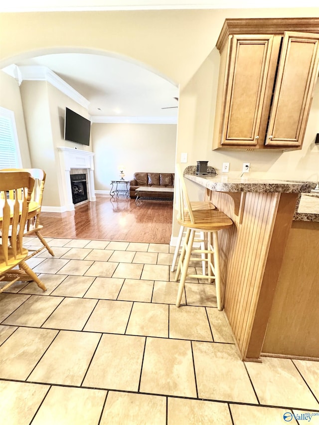 kitchen with light tile patterned floors, arched walkways, crown molding, a kitchen bar, and a fireplace