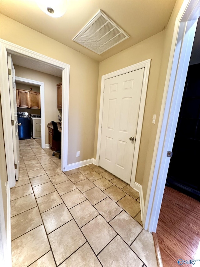 corridor with light tile patterned floors, baseboards, visible vents, and washer / clothes dryer