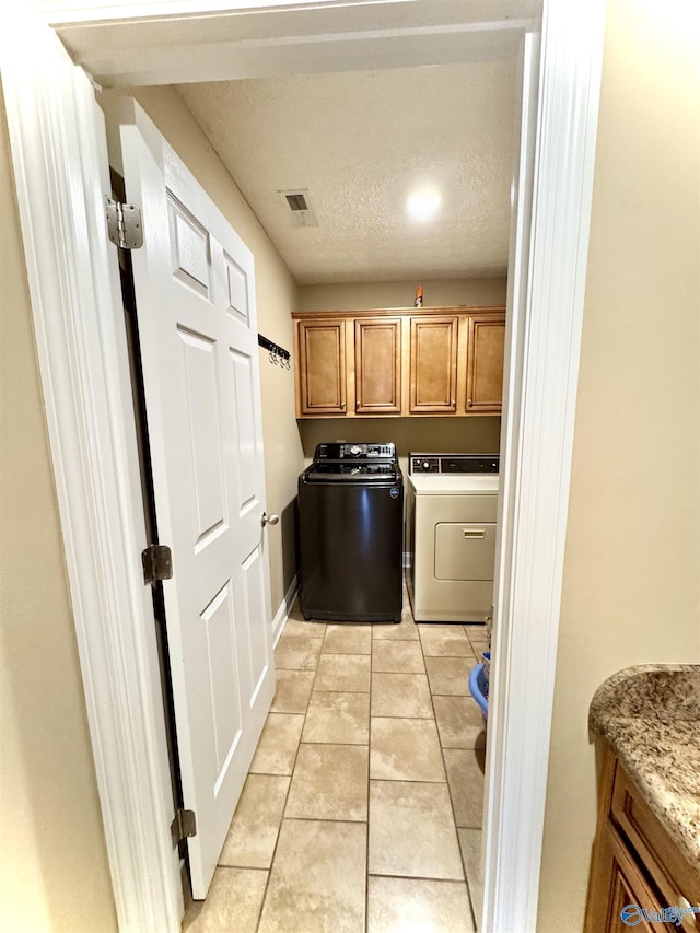 laundry room with light tile patterned floors, a textured ceiling, visible vents, independent washer and dryer, and cabinet space