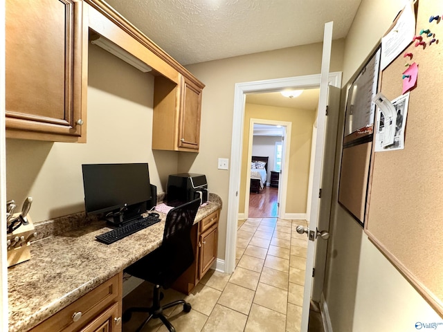 office with built in study area, a textured ceiling, baseboards, and light tile patterned floors