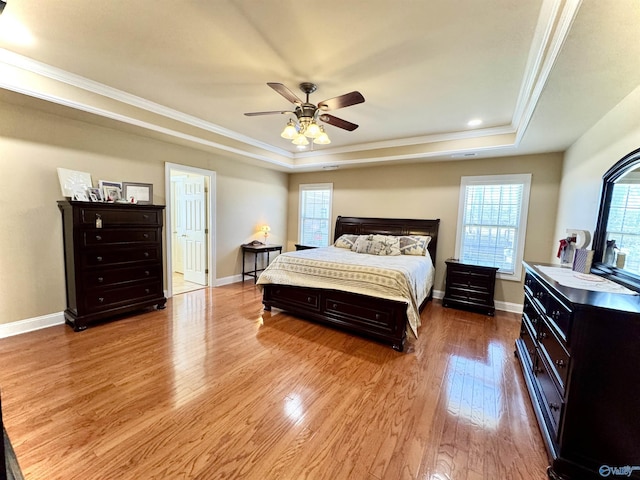 bedroom with a ceiling fan, baseboards, ornamental molding, a tray ceiling, and light wood finished floors